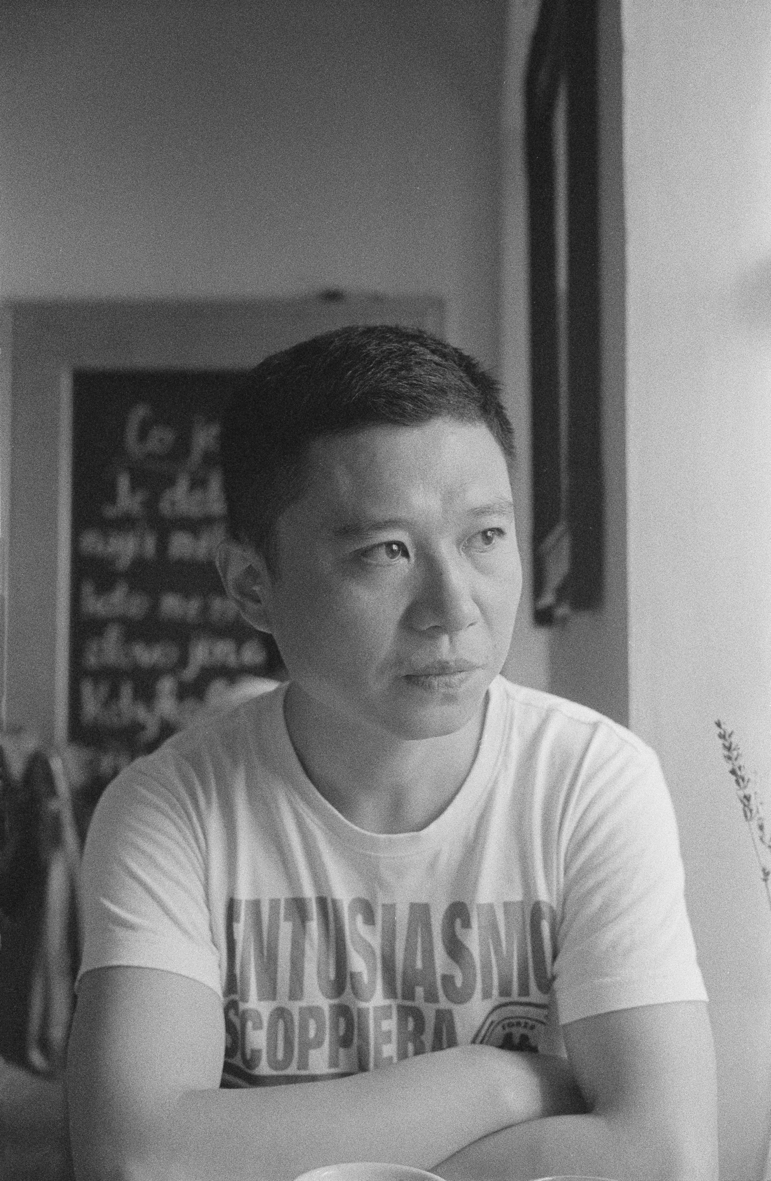 Yi Bai, portrait en noir et blanc : bras croisés, le regard porté hors du cadre